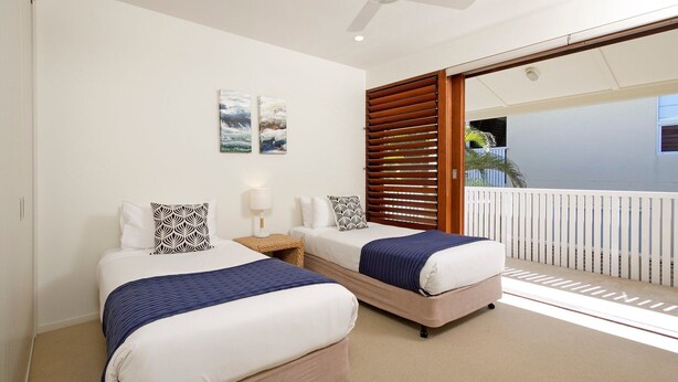 A hotel room with two beds, a ceiling fan, and a balcony with a white railing. - Hale Lani 2 - Oceanview Penthouse Paradise (Sunshine Beach)