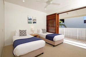 Une chambre d’hôtel avec deux lits, un ventilateur de plafond et un balcon doté d’une balustrade blanche.