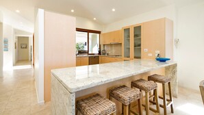 A modern kitchen with a marble countertop, wooden cabinets, and bar stools. - Hale Lani 2 - Oceanview Penthouse Paradise (Sunshine Beach)