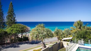 A residential area with a clear view of the ocean, a swimming pool, and a road with a sidewalk. - Hale Lani 2 - Oceanview Penthouse Paradise (Sunshine Beach)
