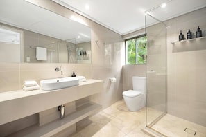 A modern bathroom with a large mirror, a white sink, a toilet, and a glass-enclosed shower area.