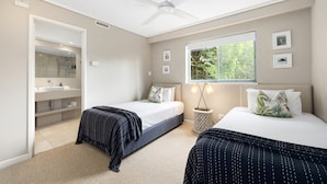 Une chambre avec deux lits, un ventilateur de plafond, une fenêtre donnant sur un espace verdoyant, et une salle de bain avec douche et lavabo.