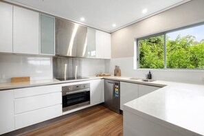 A modern kitchen with white cabinetry, stainless steel appliances, and a window providing a view of greenery.