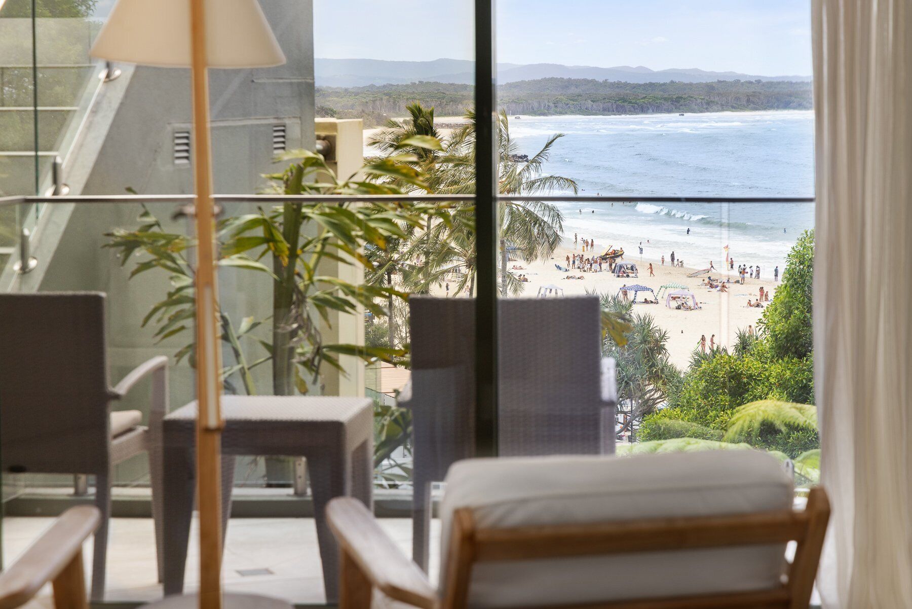 A balcony with a view of a beach, a chair, and a table.