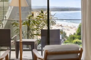 A balcony with a view of a beach, a chair, and a table.
