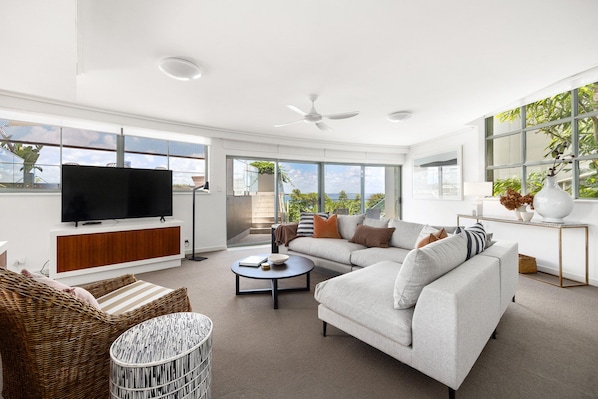 A modern living room with a sectional sofa, a flat-screen TV, and a ceiling fan.