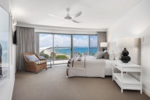 A hotel room with a bed, a seating area, a TV, and a view of the beach.