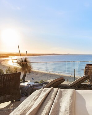 A beach view from a balcony with wicker furniture and a large vase.