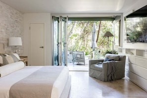 A bedroom with a bed, a chair, a lamp, and a view of the outdoors.