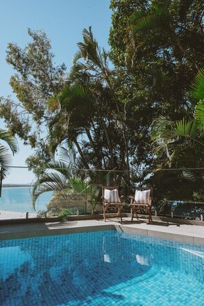 A swimming pool with two wooden chairs and a view of the sea.