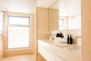 A bathroom with a large window, a white sink, and a mirror.