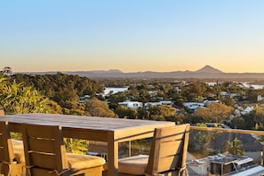 A wooden table and chairs on a balcony overlooking a residential area with houses and a mountain in the distance.
