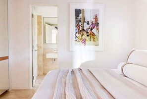 Quarto de hotel com uma cama, banheiro com espelho e uma moldura na parede.