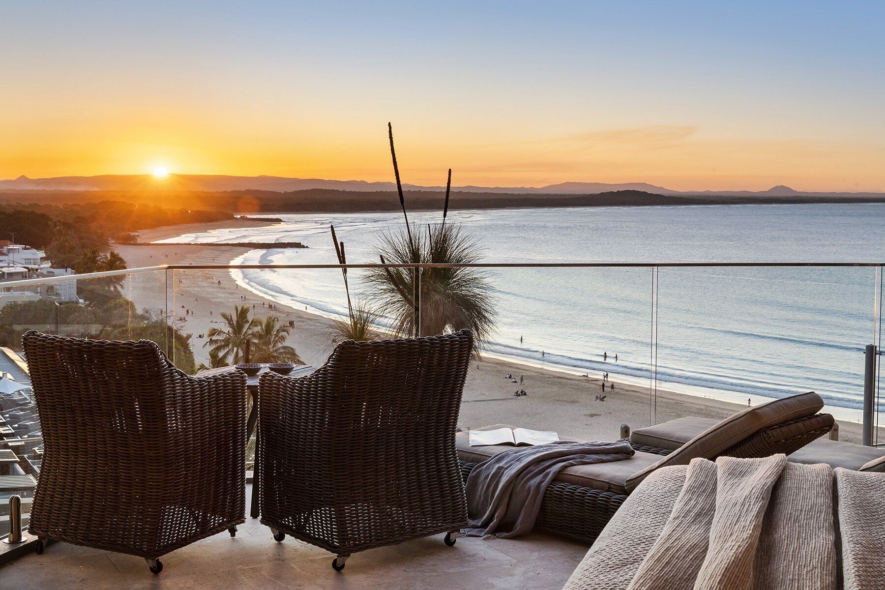 A balcony with wicker chairs and a view of the beach at sunset.