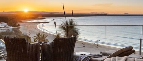 A balcony with wicker chairs and a view of the beach at sunset.
