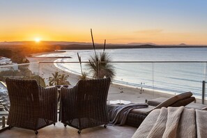 Varanda com cadeiras de vime e vista para a praia ao pôr do sol.
