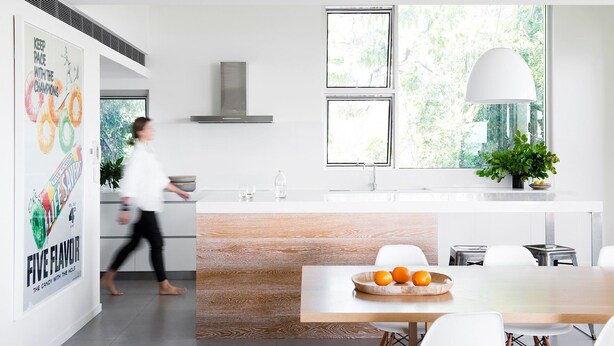 Una cocina moderna con una isla central, un comedor y un amplio ventanal con vistas a zonas verdes.