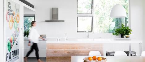 Una cocina moderna con una isla central, un comedor y un amplio ventanal con vistas a zonas verdes.