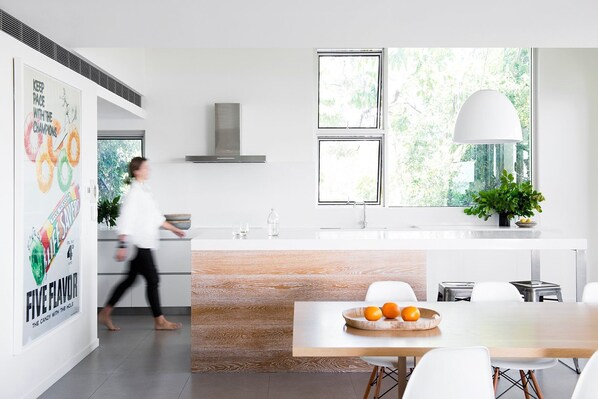 A modern kitchen with a central island, a dining area, and a large window with a view of greenery.