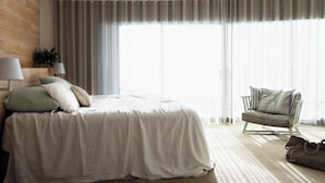 Un dormitorio con una cama, una silla, una lámpara y una ventana con cortinas.