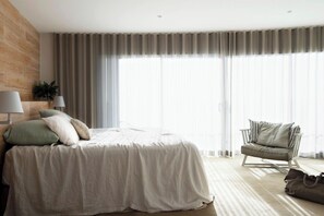 A bedroom with a bed, a chair, a lamp, and a window with curtains.