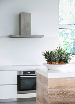 A modern kitchen with a built-in oven, a stainless steel range hood, and a wooden accent wall.