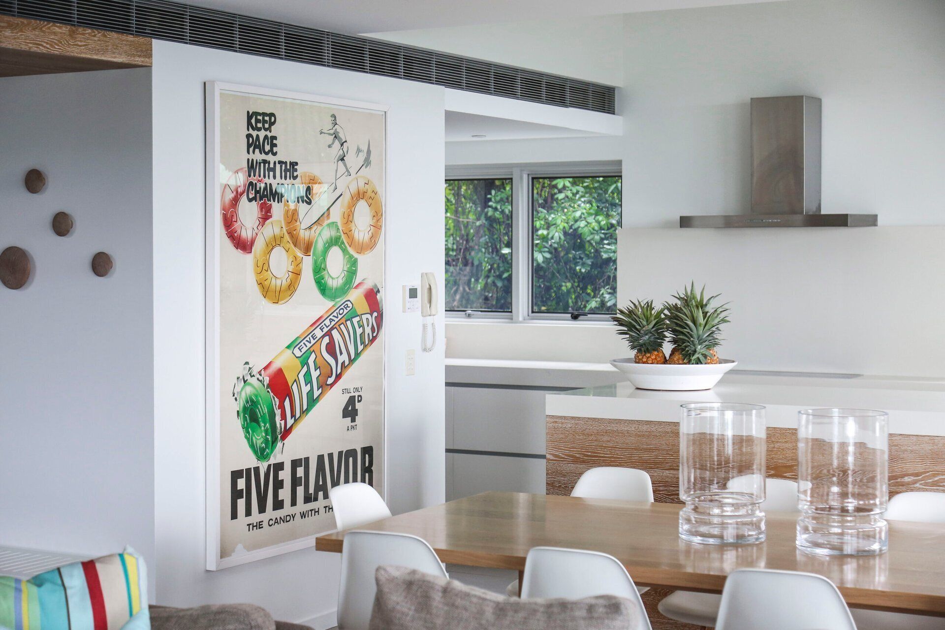 Una cucina moderna con zona pranzo, con un poster di una barretta di cioccolato, una pianta in vaso e vista su del verde all'esterno.