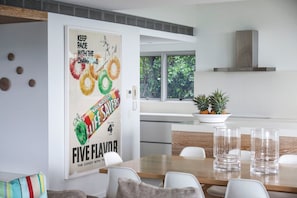 A modern kitchen with a dining area, featuring a poster of a candy bar, a potted plant, and a view of greenery outside.