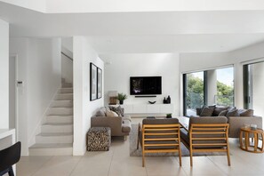 Un soggiorno moderno con una scala, una TV a schermo piatto e un'ampia finestra che si affaccia sul verde.