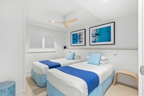 Ein Schlafzimmer mit zwei Betten, einem Deckenventilator und zwei gerahmten Bildern an der Wand.