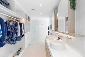 Features a spacious walk-in closet with shelves and hanging space, a large mirror, and two sinks.