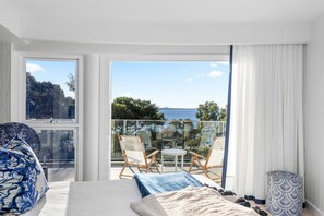 A hotel room with a bed, a balcony with a table and chairs, and a view of the sea.