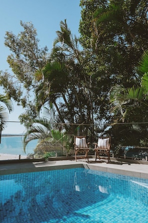 A swimming pool with two wooden chairs and a view of the sea.