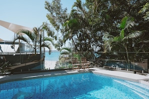 Una piscina con vistas a la playa y palmeras.