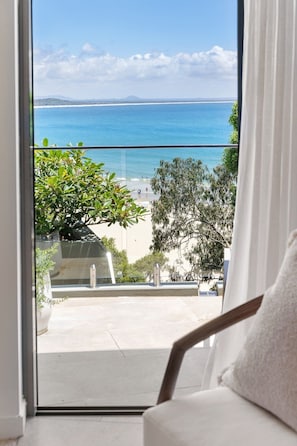 Vista desde un balcón con vista a una playa, cielos despejados y mar tranquilo.