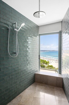 A bathroom with a shower, a view of the beach, and a tiled floor.