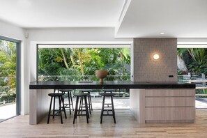 A modern kitchen with a large island, bar stools, and a view of lush greenery outside.