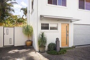 A modern two-story house with a white exterior, a wooden front door, and a garage door. - The Islander - Tropical Noosa Getaway (Noosa)