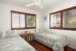 Un dormitorio con dos camas individuales, ventilador de techo y ventanas con persianas de madera.