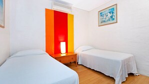 Een hotelkamer met twee enkele bedden, een nachtkastje, een lamp, een airconditioner en een schilderij aan de muur.