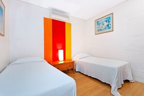 Ein Hotelzimmer mit zwei Einzelbetten, einem Nachttisch, einer Lampe, einer Klimaanlage und einem Bild an der Wand.