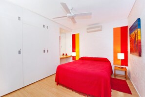A hotel room with a bed, a ceiling fan, a nightstand, a lamp, and a painting on the wall.