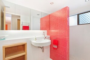 A modern bathroom with a white sink, a red tiled shower wall, and a wooden vanity.