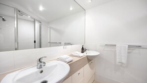 A modern bathroom with a large mirror, a sink, and a shower area. - Kareka - Little Cove Serenity with Pool (Little Cove)