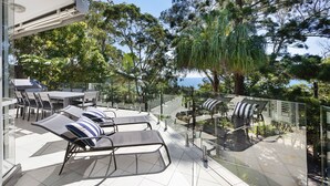 An outdoor patio with a dining table and chairs, lounge chairs with cushions, and a view of the sea. - Kareka - Little Cove Serenity with Pool (Little Cove)