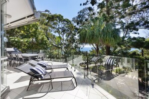 An outdoor patio with a dining table and chairs, lounge chairs with cushions, and a view of the sea. - Kareka - Little Cove Serenity with Pool (Little Cove)