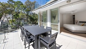 A modern outdoor dining area with a long table and chairs, adjacent to a bedroom with a bed and a nightstand. - Kareka - Little Cove Serenity with Pool (Little Cove)