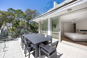 A modern outdoor dining area with a long table and chairs, adjacent to a bedroom with a bed and a nightstand. - Kareka - Little Cove Serenity with Pool (Little Cove)