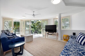 Ein modernes Wohnzimmer mit einer Couch, einem Couchtisch, einem Fernseher auf einem Schrank und einem Deckenventilator.