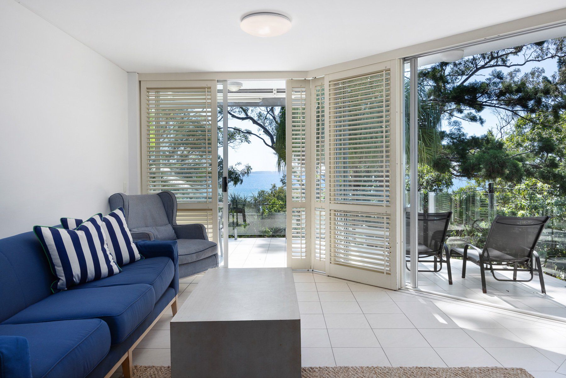 A modern living room with a sofa, a coffee table, and a view through a glass door to an outdoor seating area.